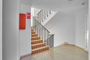 Un escalier, un extincteur rouge fixé au mur, une porte blanche et un sol ciré.