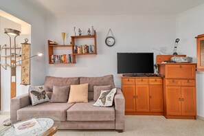 Un salon comprenant un canapé, une table basse, une bibliothèque, un téléviseur et des meubles de rangement en bois.