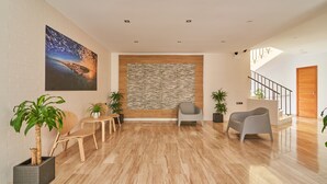 Un vestíbulo amplio con suelo de madera, pared de piedra y un cuadro grande. Se observan dos sillas y una planta en maceta.