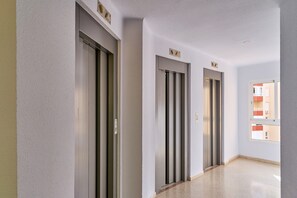 Un couloir avec trois ascenseurs, un sol impeccable et une fenêtre donnant sur des immeubles.
