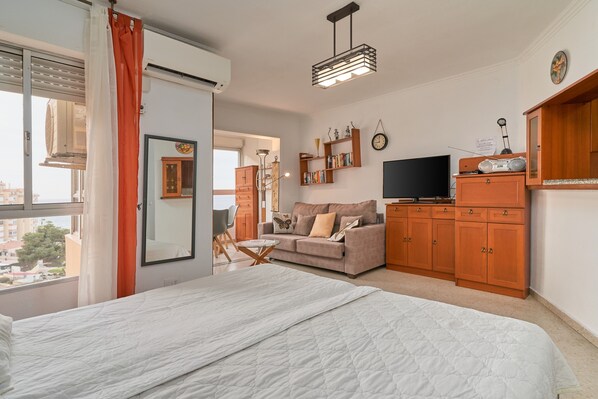 Un dormitorio con cama, sofá, televisión y armarios de madera.