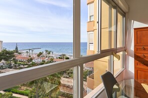 Een balkon met uitzicht op zee, een glazen tafel en houten kasten.