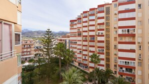 Un edificio residencial de varios pisos con balcones, una escalera central y vistas a montañas distantes.