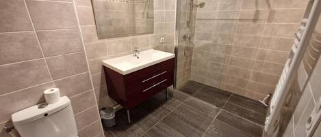 A bathroom with a toilet, sink, vanity, and shower area.