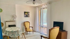 A room with a dining table, two chairs, a television, and a window with curtains.