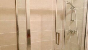 A glass-enclosed shower with a handheld showerhead and a wall-mounted faucet.