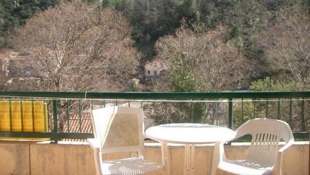 A balcony with two white plastic chairs and a table, overlooking a mountainous landscape with trees and a building in the distance. - Cozy Studio for 2 with Balcony, Wi-Fi near Thermes, Amélie-les-Bains (Amélie-les-Bains-Palalda)