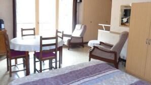A room with a bed, a dining table with chairs, a sofa, a wardrobe, and a window with curtains. - Cozy Studio for 2 with Balcony, Wi-Fi near Thermes, Amélie-les-Bains (Amélie-les-Bains-Palalda)