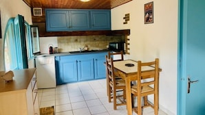 A compact kitchen with blue cabinets, a wooden dining table, and a tiled floor.