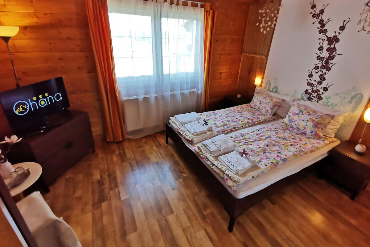 Una habitación de madera con una cama, un televisor y un ventanal con cortinas.