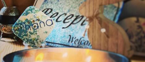 A candle in a blue container with a wooden sign above it that reads "Welcome."