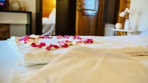 Una cama con pétalos de rosa y velas, puertas de madera y una mesita con un jarrón.