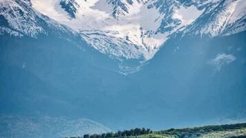 A mountainous landscape with snow-capped peaks and a valley with green fields and trees.