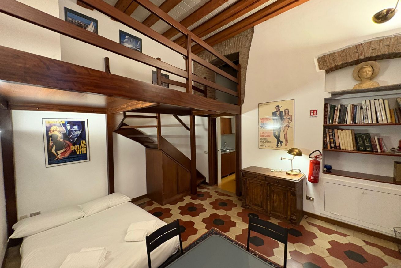 A room with a bunk bed, a desk with a lamp, a bookshelf, and a staircase.