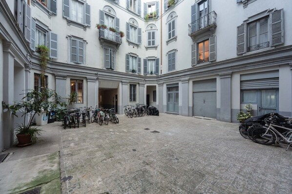 A courtyard with multiple bicycles parked, a potted plant, and a building with balconies.