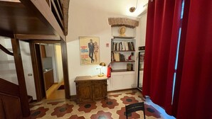Ein Zimmer mit Fliesenboden, einem Schreibtisch mit Lampe, einem Bücherregal und einem roten Vorhang.