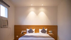 A bedroom with a wooden headboard, a large bed with white bedding, two bedside tables, and a nightstand. - Iris Lite Corbett (Ramnagar)