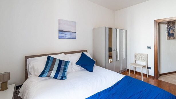 Een slaapkamer met een bed, een kledingkast, een stoel en een schilderij aan de muur.