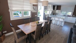 A dining area with a wooden table and wicker chairs, a kitchen with white cabinets, and a grey sofa. - MARKAIDA HOUSE WITH POOL (Mungia)