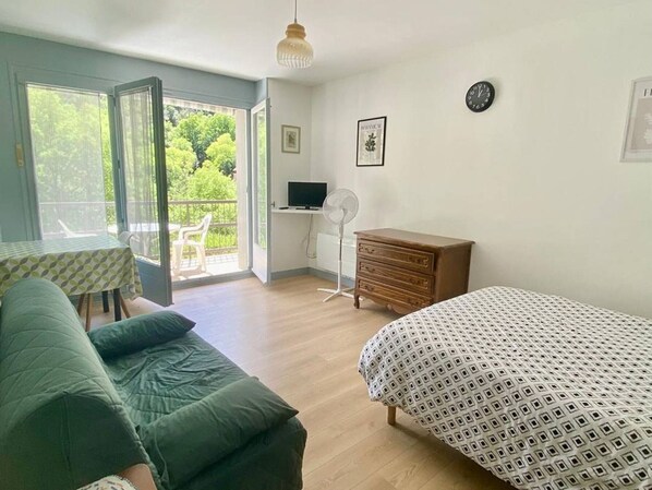 Une pièce comprenant un lit, un bureau avec un ordinateur, une commode, une chaise et une table recouverte d’une nappe.