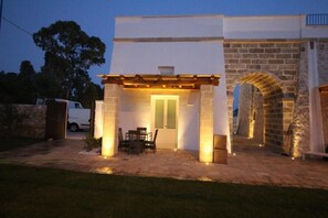 A covered patio with a table and chairs, a stone archway, and a white building with a door. - DIMORA LE SITE (Racale)