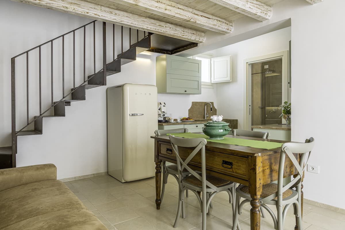 A kitchen with a dining table, chairs, a refrigerator, and a staircase.