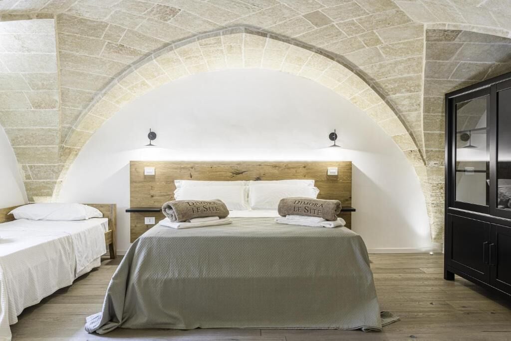 Un dormitorio con techo de arco de piedra, cabecera de madera, dos camas y un armario negro.