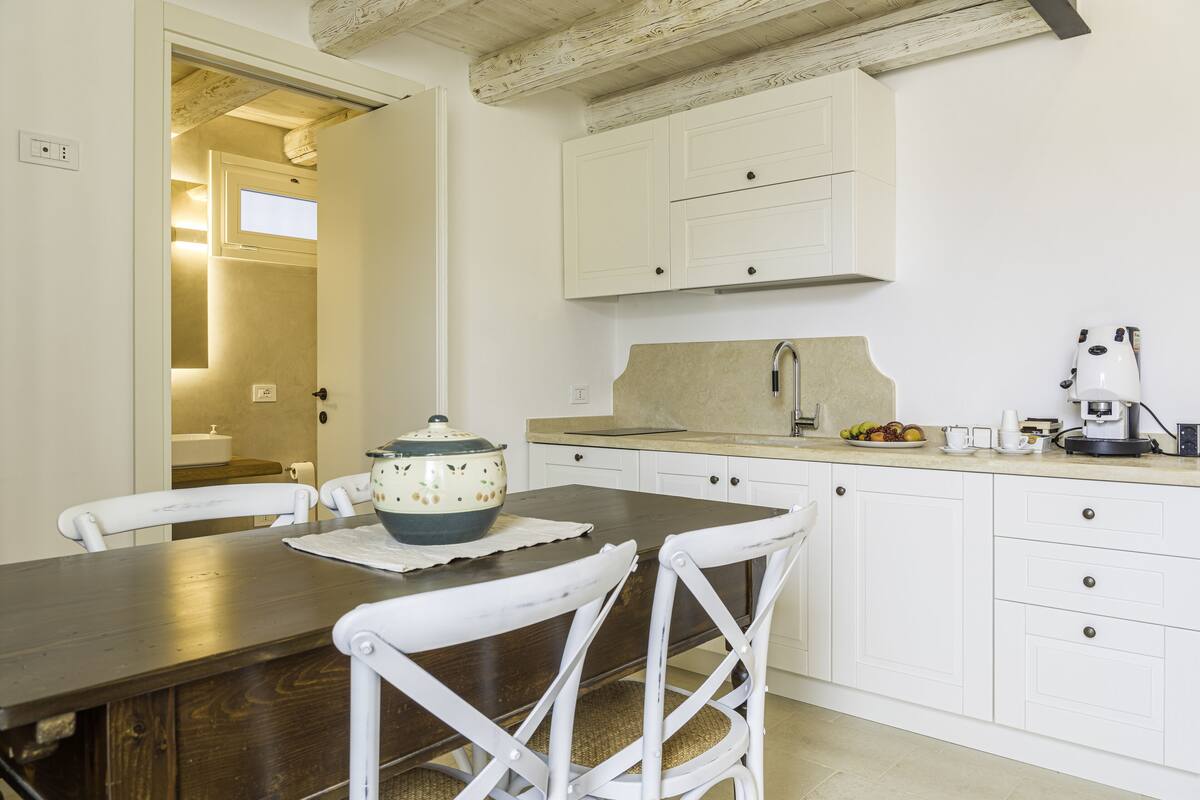 A kitchen with white cabinets, a wooden table, and a coffee maker.