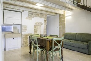 A dining area with a wooden table and chairs, a stone wall, a green sofa, and a white cabinet with a sink. - DIMORA LE SITE (Racale)