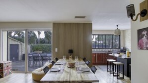 A modern dining area with a long wooden table set for four, a kitchen with dark cabinets, and a large window providing natural light. - la Choupette by Interhome (Saint Cyr sur mer Les Lecques)