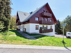 A two-story chalet with a sloped roof, wooden balconies, and a paved driveway.