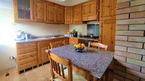 A kitchen with wooden cabinets, a granite countertop, a stove, and a bowl of fruit on the table.
