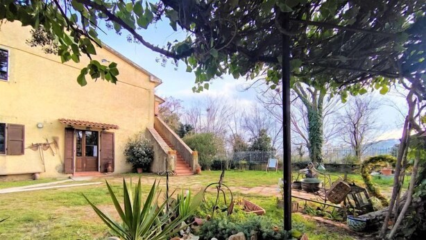 A rustic house with a garden featuring a stone pathway, potted plants, and a small fountain.