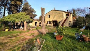 A rustic house with a garden, a pergola, and a staircase leading to the upper floor.