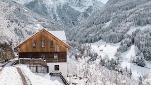 A wooden cabin with a sloped roof, surrounded by snow-covered mountains and trees. - David am Buchhammerhof by Interhome (Kaunerberg)
