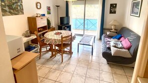 Una sala de estar con sofá, una mesa de comedor con sillas, televisión y balcón con vistas.