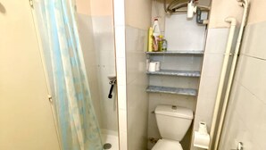 Un baño pequeño con ducha, inodoro y repisas con artículos de aseo.