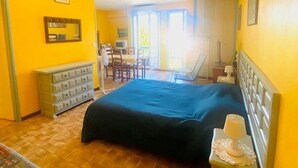 Una habitación con cama, cómoda, silla y escritorio con computadora.
