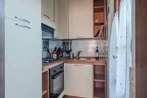 A compact kitchen with white cabinets, a stove, oven, and a sink.