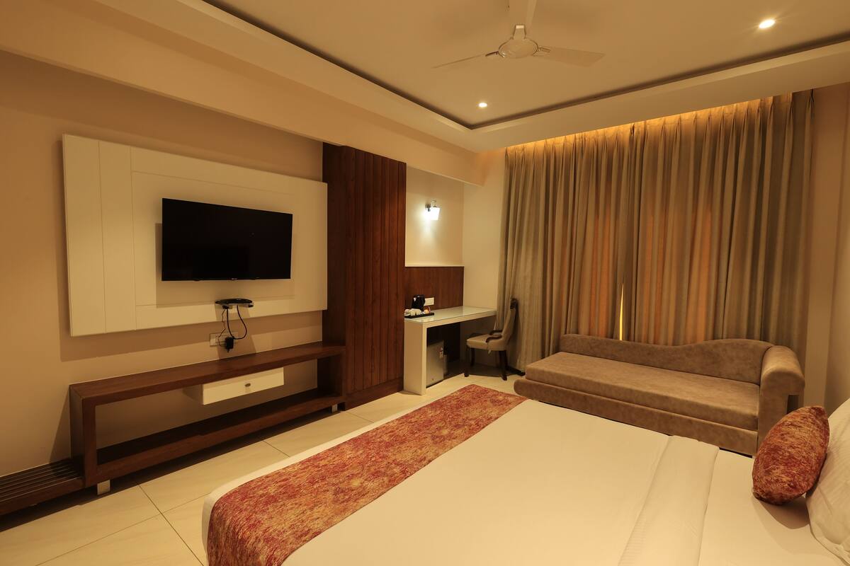 A modern hotel room with a large bed, a desk, a sofa, and a TV mounted on the wall.