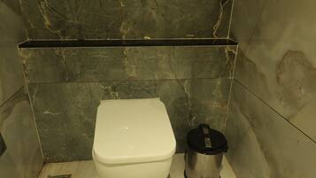 A bathroom with a toilet, a trash bin, and a shower area.
