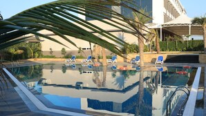 Une piscine à débordement avec des chaises longues, des palmiers et un bâtiment moderne en arrière-plan.