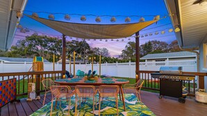 En udendørs terrasse med et bord, stole, grill og en parasol i tiki-stil.