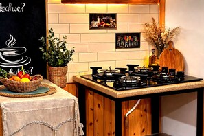 Una cocina con estufa a gas, una cesta de frutas, una planta en maceta e imagen colgada en la pared.