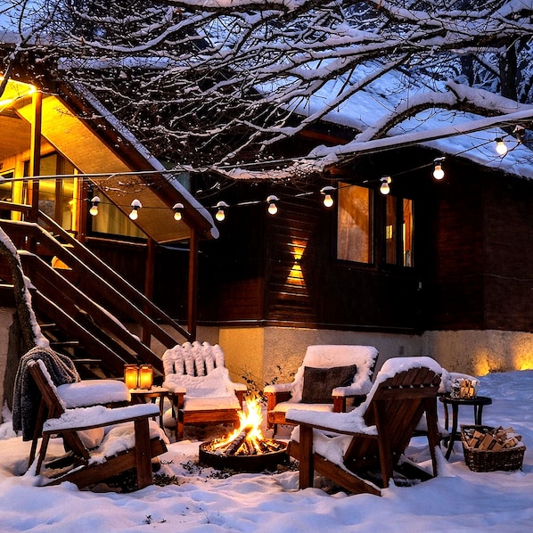 A snow-covered outdoor seating area with a fire pit, wooden chairs, and a staircase leading to a building. - Wooden nice house (Tbilisi)