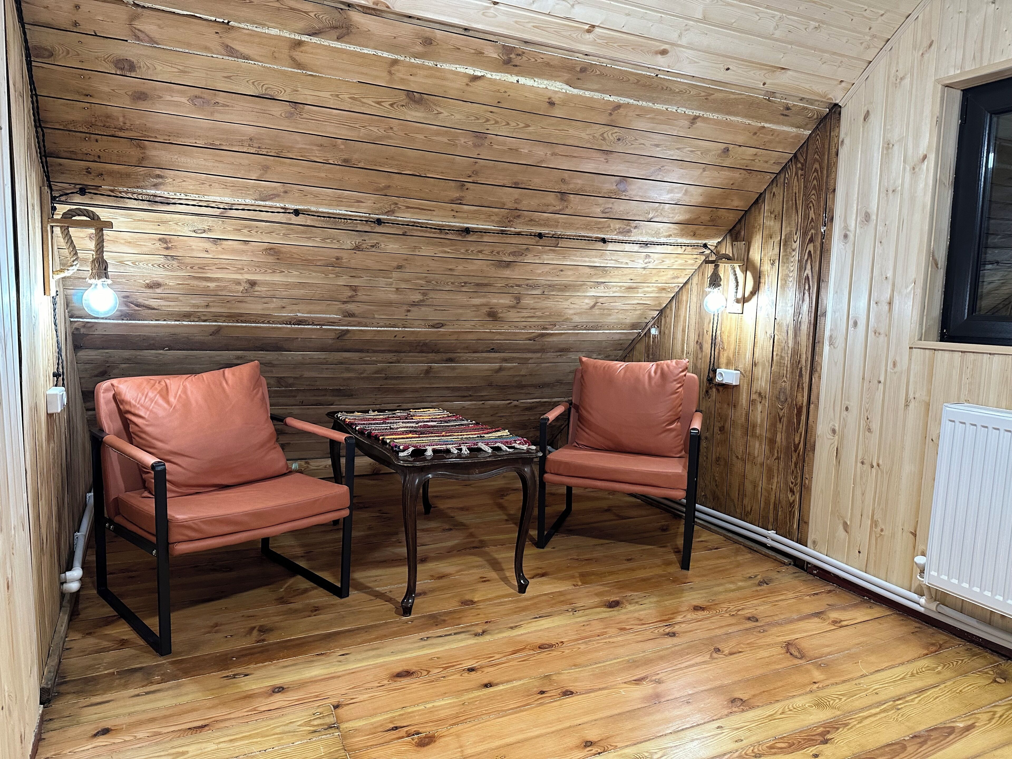 A cozy attic room with wooden walls and a sloped ceiling. There are two leather chairs and a small table with a woven mat.