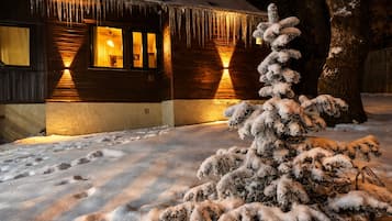 A cabin with a snow-covered ground, icicles hanging from the roof, and a snow-covered tree in front.