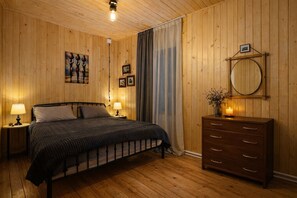 Quarto com painéis de madeira, uma cama, duas luminárias de cabeceira, um cômoda, um espelho e um quadro na parede.