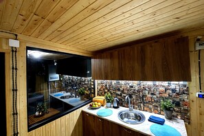 A kitchen with wooden cabinets, a stone backsplash, and a stainless steel sink. - Wooden nice house (Tbilisi)
