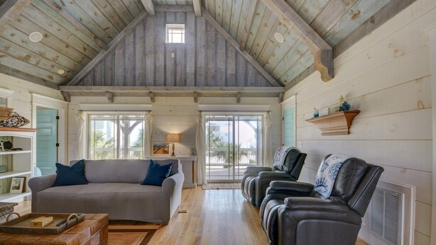 A spacious living room with a high ceiling, wooden beams, a sofa, a loveseat, and a coffee table.